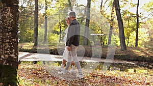 couple, man and pregnant wife are holding hands and walking in the autumn park on sunset. Happy family enjoying