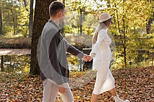 couple, man and pregnant wife are holding hands and walking in the autumn park on sunset. Happy family enjoying