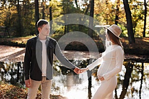 couple, man and pregnant wife are holding hands and walking in the autumn park on sunset. Happy family enjoying