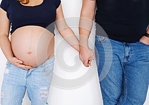 A couple, a man and a pregnant woman stand near a white wall and hold hands. The concept of support and love in the