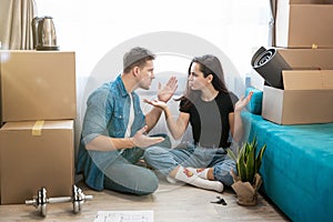 Couple man and woman have argument sitting on the floor during unpacking boxes, woman closes her ears, man cries , moving process