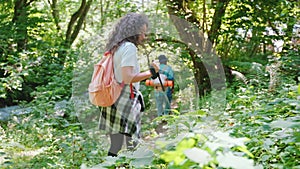 Couple man and woman hiking in wild forest with sticks by pathway.