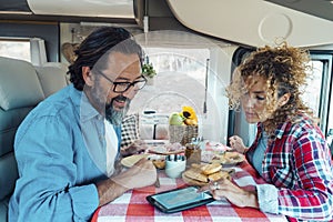 Couple man and woman inside a camper van planning next travel destination together using gps modern device on the table. Lunch