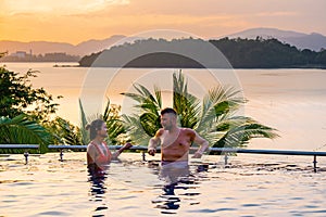 couple man and woman mid age in swimming pool on a luxury vacation in Thailand, men and Asian woman in pool looking out