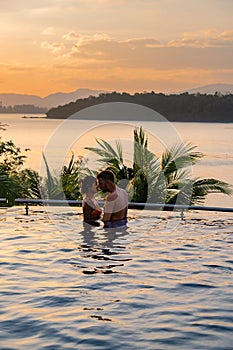 couple man and woman mid age in swimming pool on a luxury vacation in Thailand, men and Asian woman in pool looking out