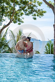 couple man and woman mid age in swimming pool on a luxury vacation in Thailand, men and Asian woman in pool looking out