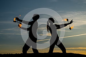 Couple of man and woman perform burning poi dance during fire performance in dark silhouettes