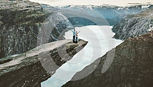 Couple Man and Woman on Trolltunga cliff raised hands mountains