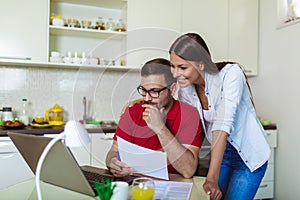 Couple managing finances, reviewing their bank accounts using laptop computer at modern kitchen