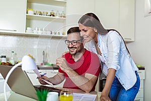 Couple managing finances, reviewing their bank accounts using laptop computer at modern kitchen