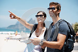 Couple, map and pointing by beach on holiday, smile and excited with search for direction. Woman, man and chart for