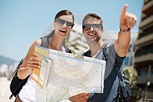 Couple, map and search with pointing on vacation, street and excited for giving direction. Woman, man and chart for