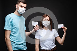 Couple in masks with empty cards. people in aseptic masks holding two blank cards with place for text. Isolate on black.
