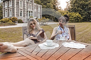 Couple of mature friendly women on vacation drinking tea and reading a book outdoors