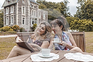 Couple of mature friendly women on vacation drinking tea and reading a book outdoors