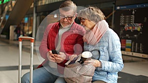 Couple of mature people consults the smartphone waiting for the train. Husband and wife waiting for the train sit on a