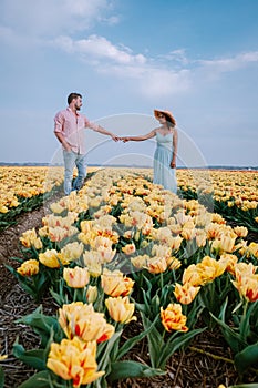 Couple men and woman in flower field in the Netherlands during Spring, orange red tulips field near Noordoostpolder