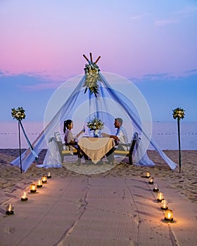 couple men and woman having romantic dinner with candle lights on the beach in Thailand, European men and Asian woman