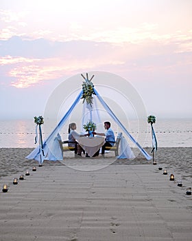 couple men and woman having romantic dinner with candle lights on the beach in Thailand, European men and Asian woman