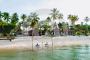 a couple of men and woman on a swing at the beach of Koh Muk Thailand