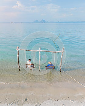 a couple of men and woman on a swing at the beach of Koh Muk Thailand