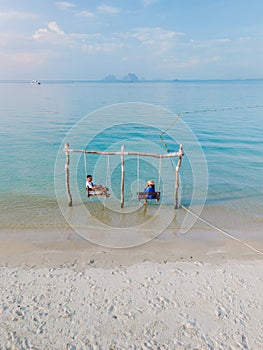 a couple of men and woman on a swing at the beach of Koh Muk Thailand