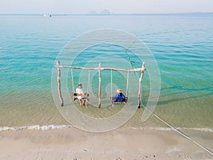 a couple of men and woman on a swing at the beach of Koh Muk Thailand