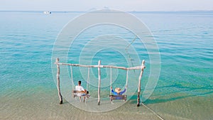 a couple of men and woman on a swing at the beach of Koh Muk Thailand