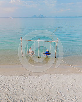 a couple of men and woman on a swing at the beach of Koh Muk Thailand