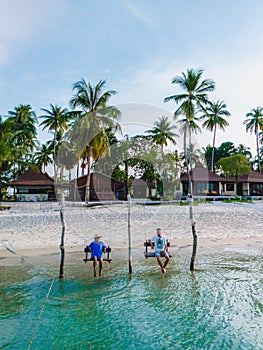 a couple of men and woman on a swing at the beach of Koh Muk Thailand