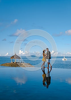 couple men and woman watching sunset on a tropical beach in Mauritius with palm trees by the swimming pool, Tropical