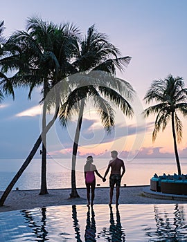 Couple of men and women relaxing by the pool in beach beds chairs, tropical pool