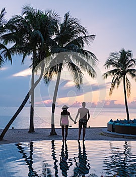 Couple of men and women relaxing by the pool in beach beds chairs, tropical pool