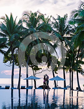 Couple of men and women relaxing by the pool in beach beds chairs, tropical pool