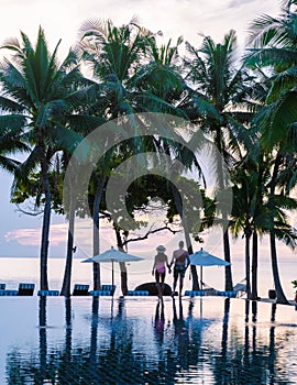 Couple of men and women relaxing by the pool in beach beds chairs, tropical pool