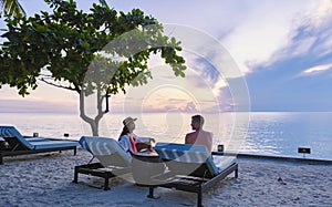 Couple of men and women relaxing by the pool in beach beds chairs, tropical pool