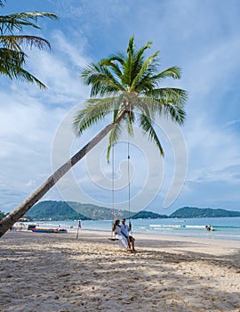 A couple of men and women on a swing under a palm tree at the beach of Patong Phuket Thailand
