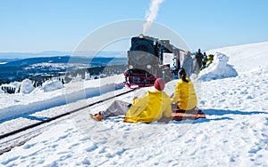 couple of men and women watching the steam train during winter in the snow in the Harz Germany