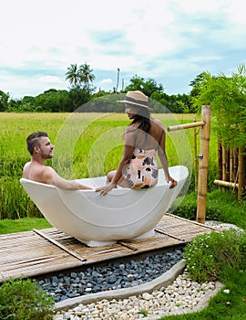 men and women in bath tub outside on vacation at a homestay in Thailand with green rice paddy field