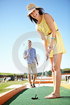 Couple, mini golf and happy woman with club, smile and hit ball on date, fun activity and freedom in sunshine. Excited