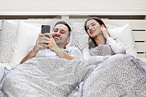 Couple with mobile phone in bed in the morning