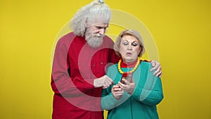 Couple of modern seniors using smartphone and talking on yellow background. Portrait of confident Caucasian man and