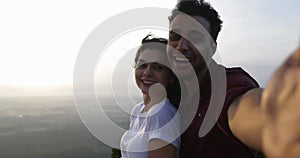 Couple on mountain top taking selfie photo at sunrise, latin man and woman happy smiling