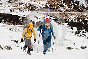 Couple of mountaineers climbing up a snowy mountain, woman carrying skis on her back