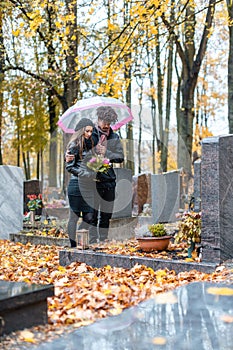 Couple mourning a deceased loved one on cemetery in fall