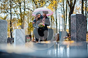 Couple mourning a deceased loved one on cemetery in fall