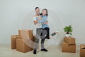 Couple moving into their new house. Woman is very glad and is hanging on her husband`s neck, hugging him.