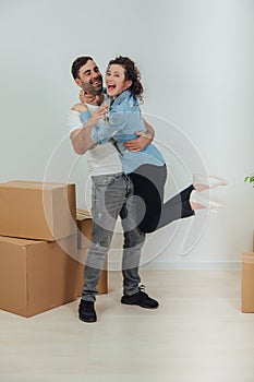 Couple moving into their new house. Woman is very glad and is hanging on her husband`s neck, hugging him.