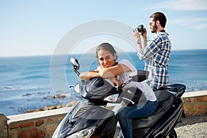 Couple near the ocean, on a scooter, taking pictutes