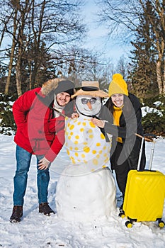 couple near snow man with valise